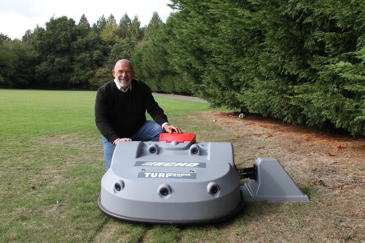 Gary Whitney beside a robotic mower on a lawn